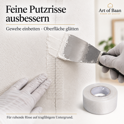 Weißes Armierungsband überbrückt einen feinen Putzriss an einer Innenwand und wird mit einem Spachtel eingearbeitet.