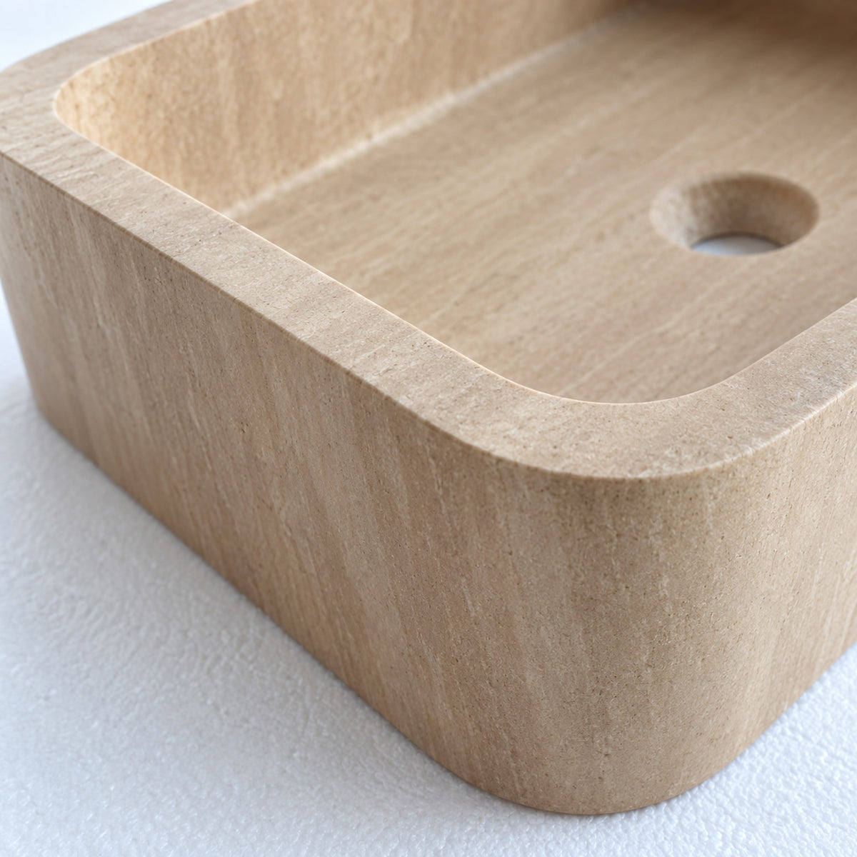 Detailansicht von Beckenrand und abgerundeter Ecke mit der beigen Travertinstruktur.
