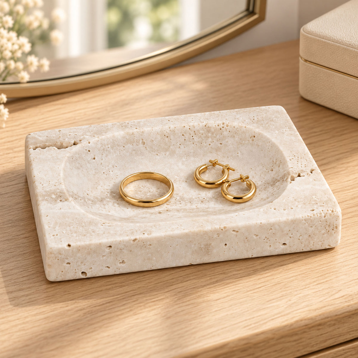 Seifenschale aus weißem Travertin mit einem goldfarbenen Ring und zwei Creolen auf einem hölzernen Schminktisch.
